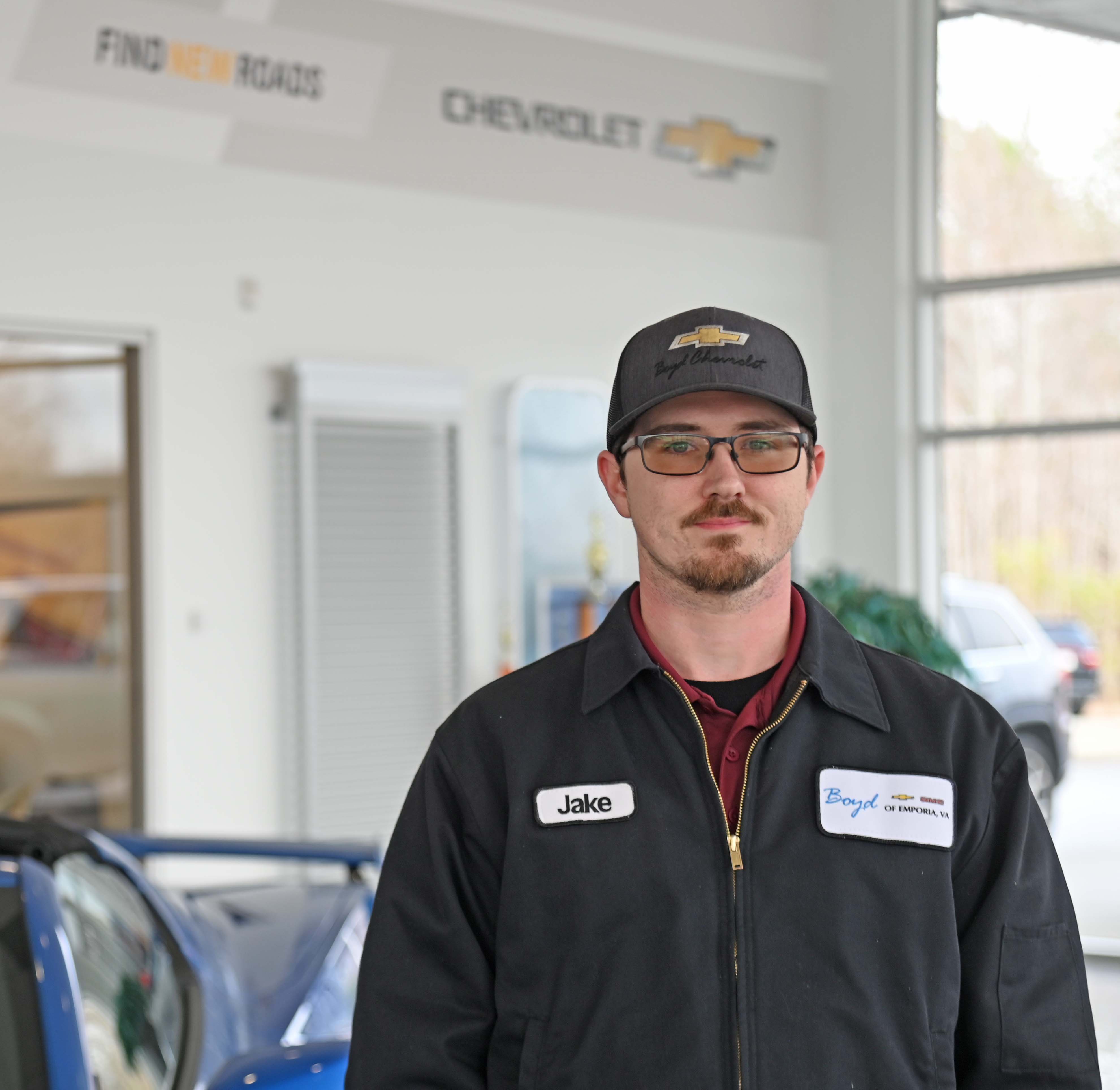 Jacob Myrick standing in front of Boyd Chevrolet sign in work jacket and hat