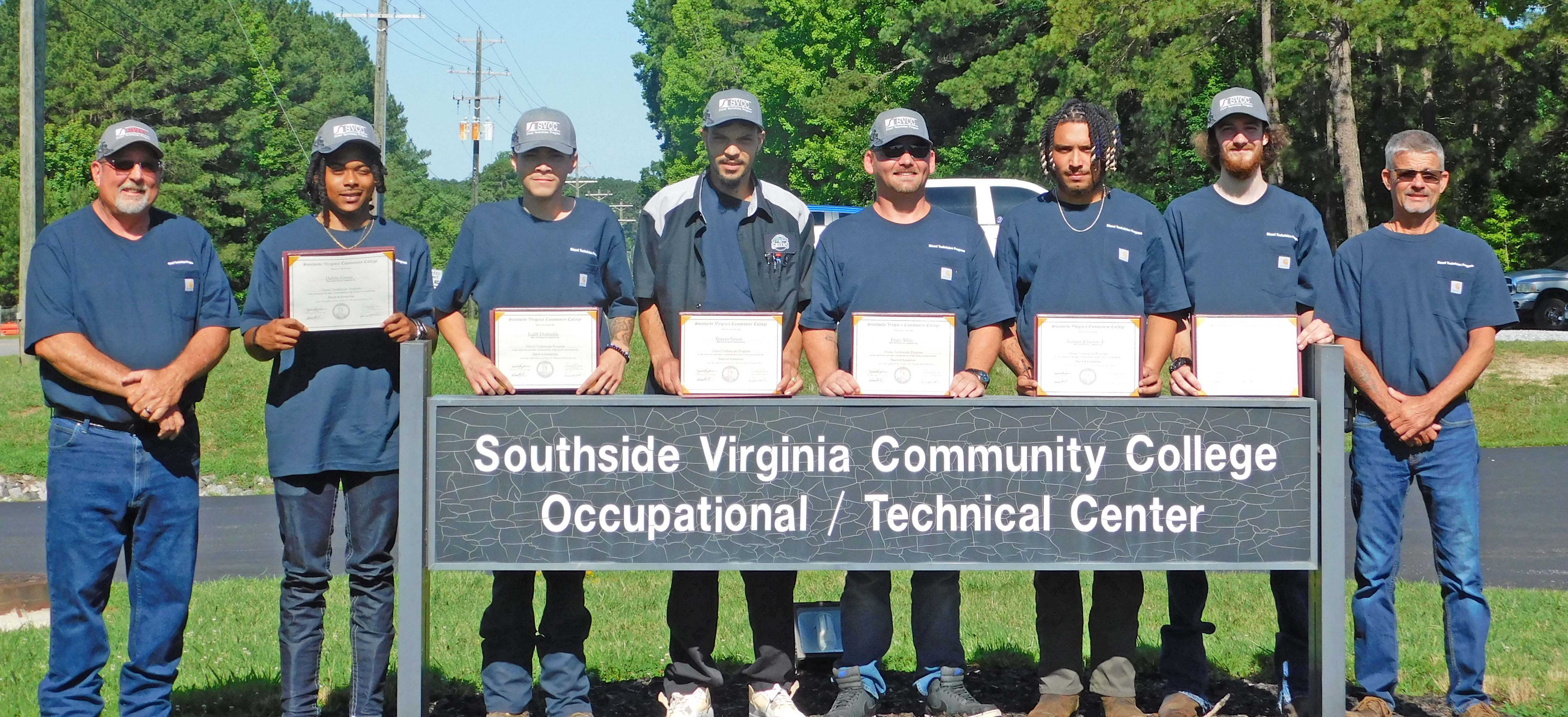 6 Diesel program graduates and 2 instructors standing outside by the Southside VA CC OTC sign