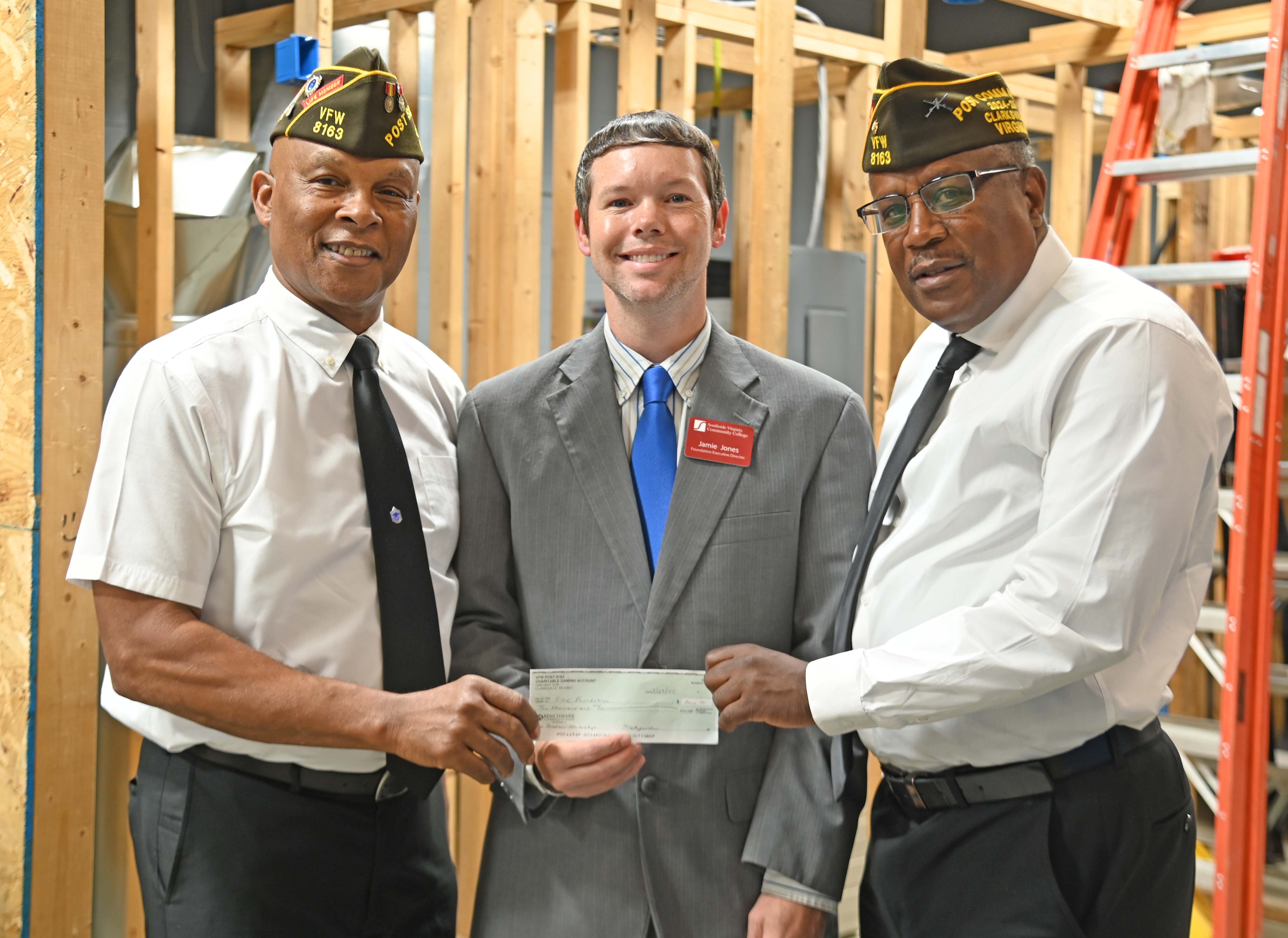 VFW Post Commander and Vice Commander in uniform, presenting a check to SVCC Foundation Director posing indoors with construction behind them