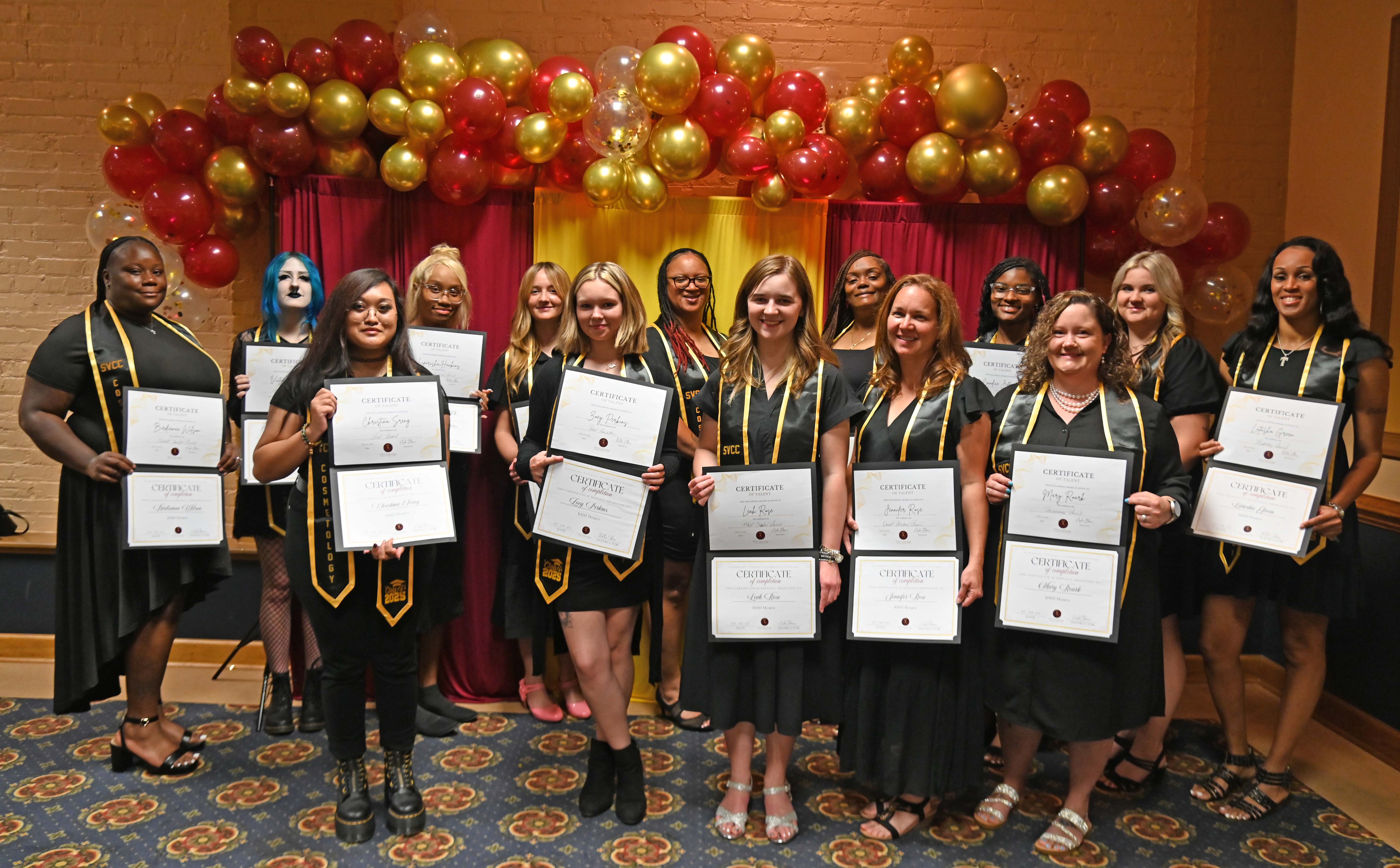 Group of cosmetology students posing on stage with certificates and balloons
