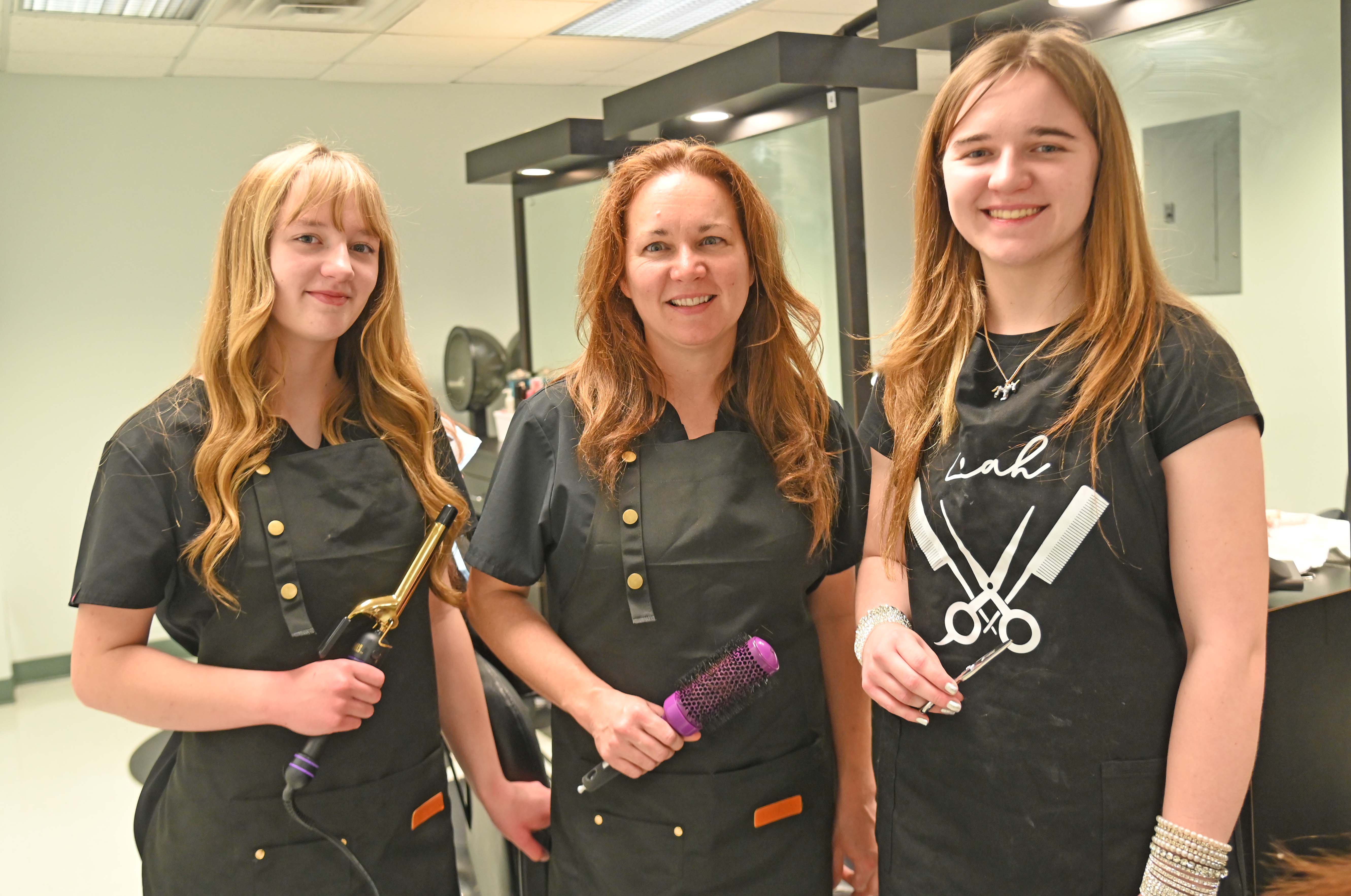 three women posing in a salon with Cosmetology tools