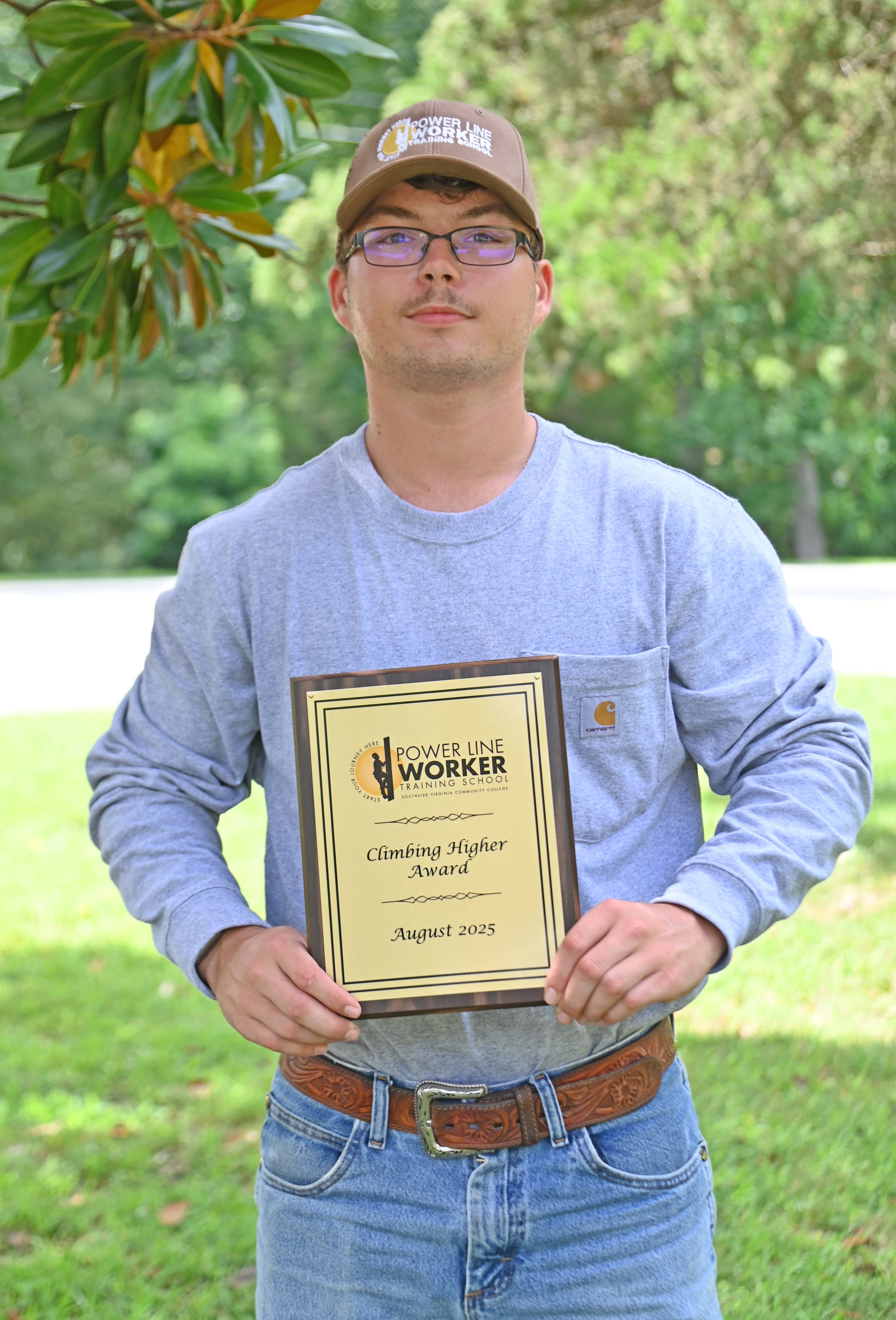 Student in hat posed outside holding a plaque