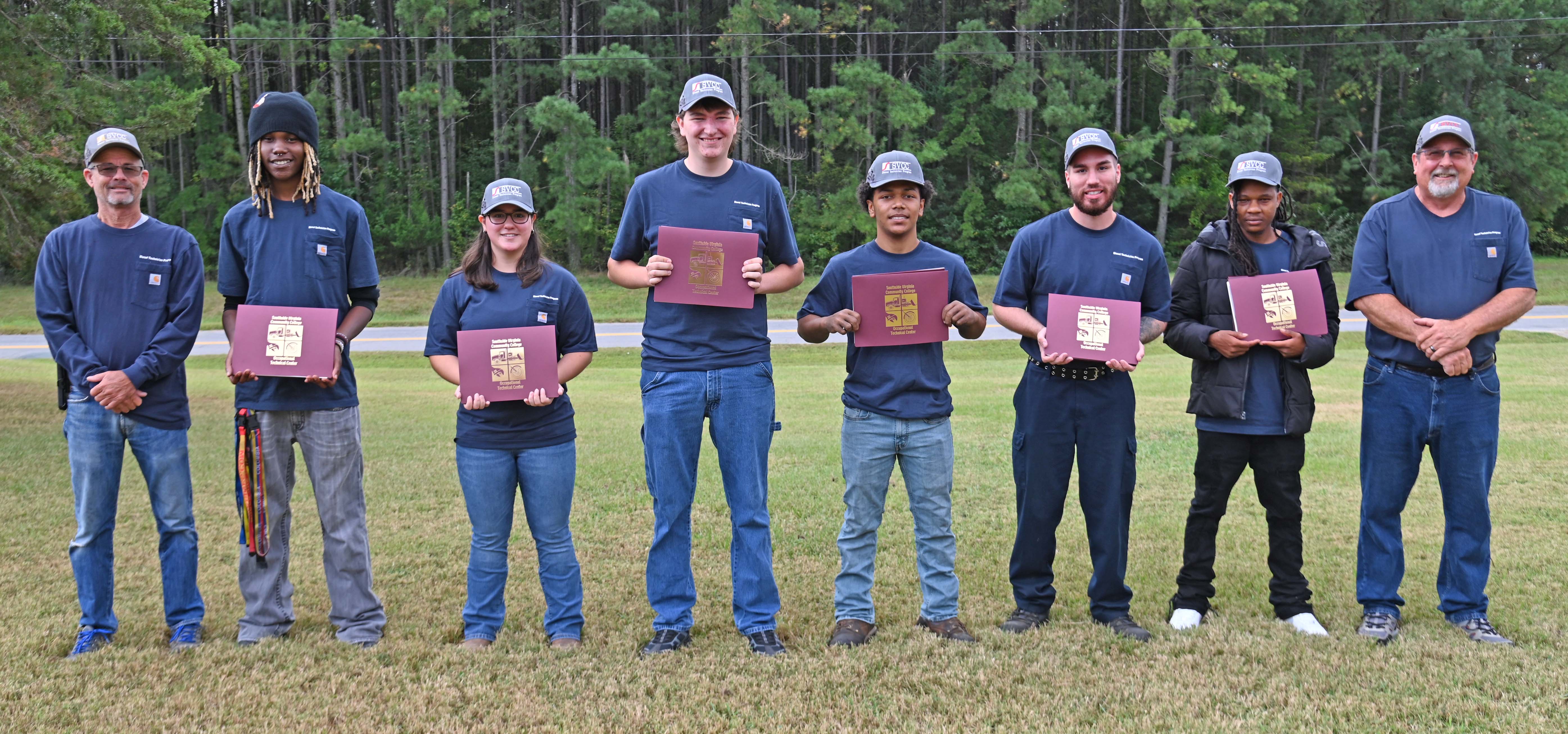 6 Diesel graduates in matching shirts holding certificates, between 2 instructors
