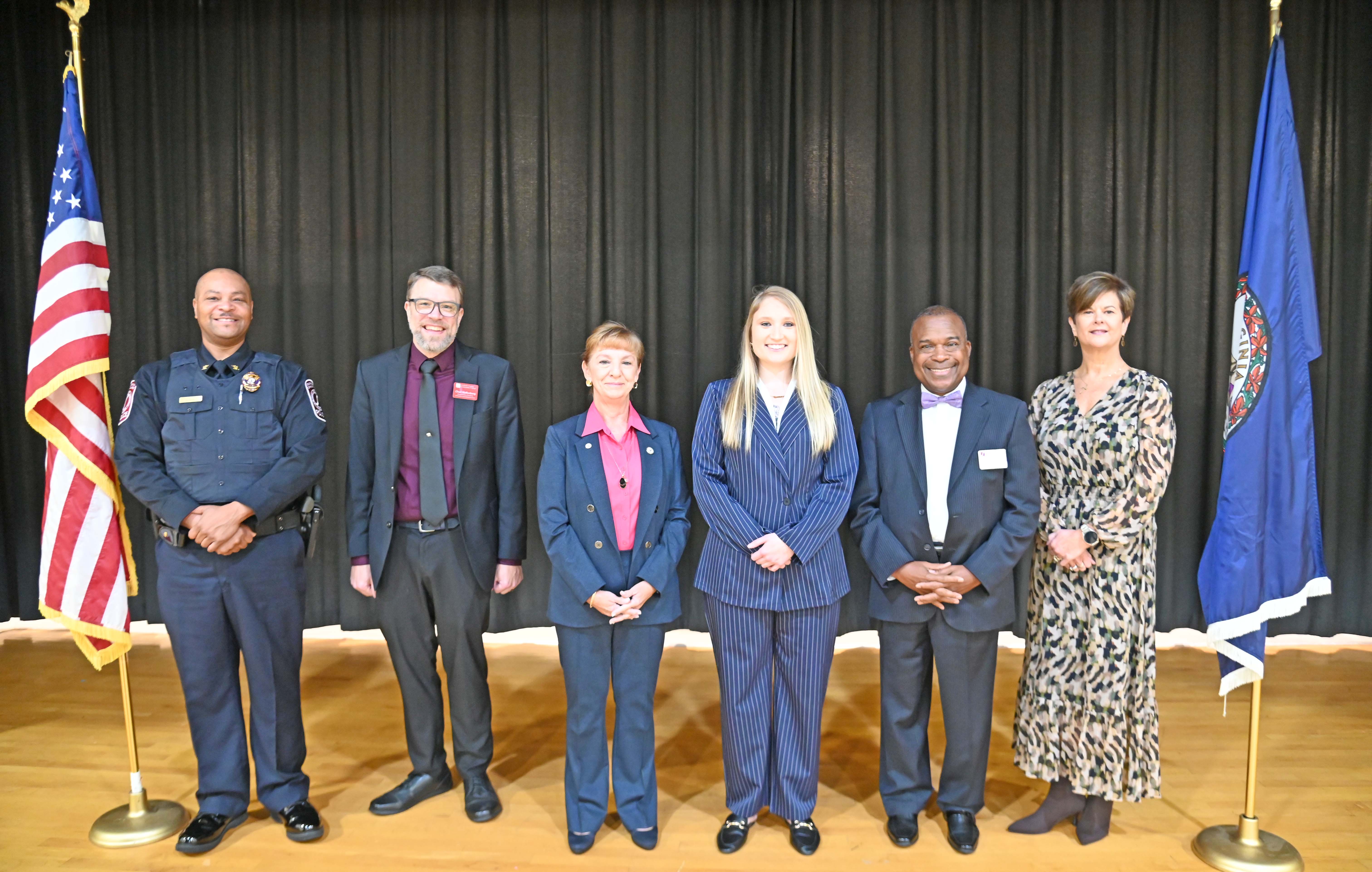 6 people standing on stage between flags