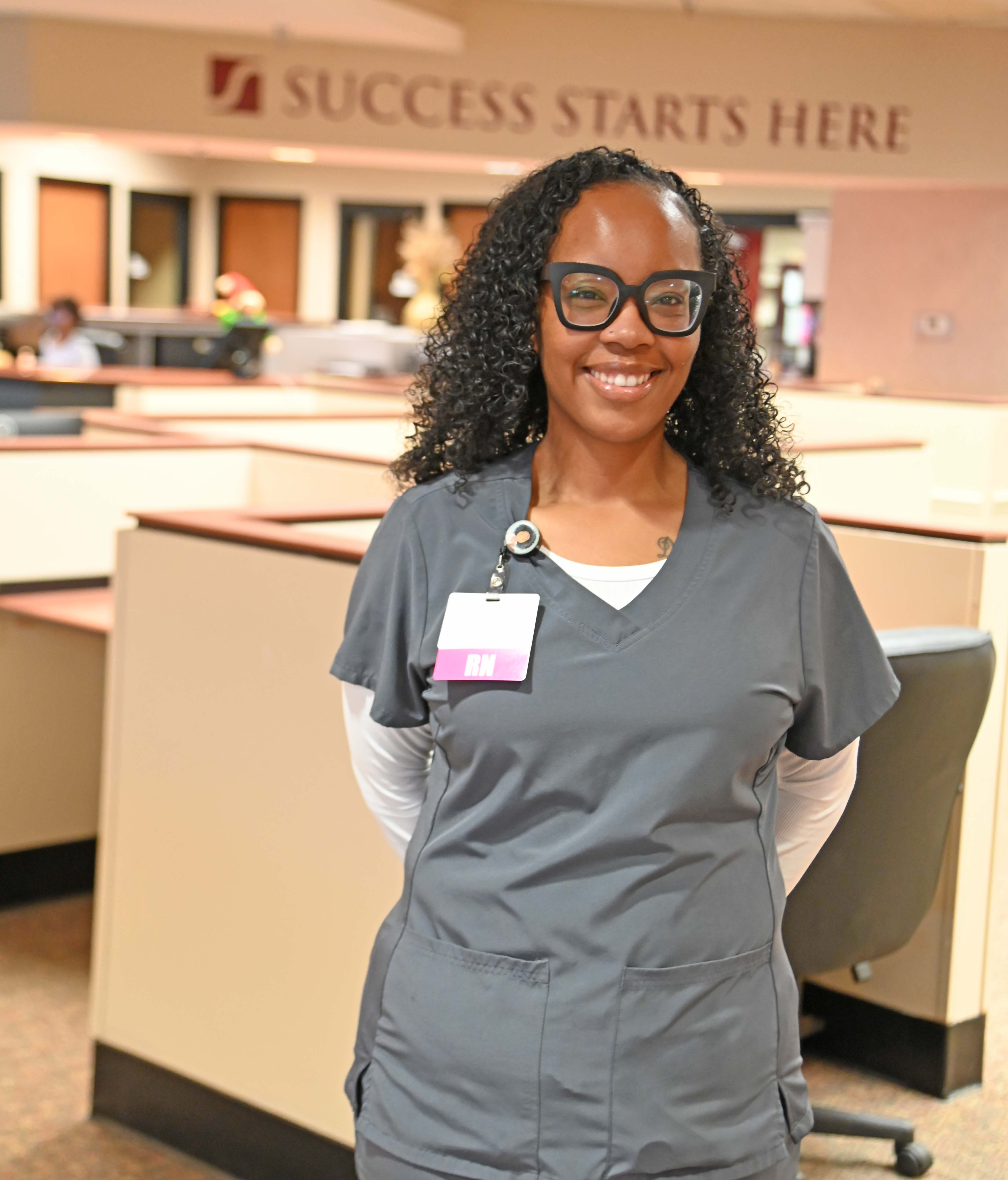 Ashley Greene wearing nursing scrubs in front of SVCC sign