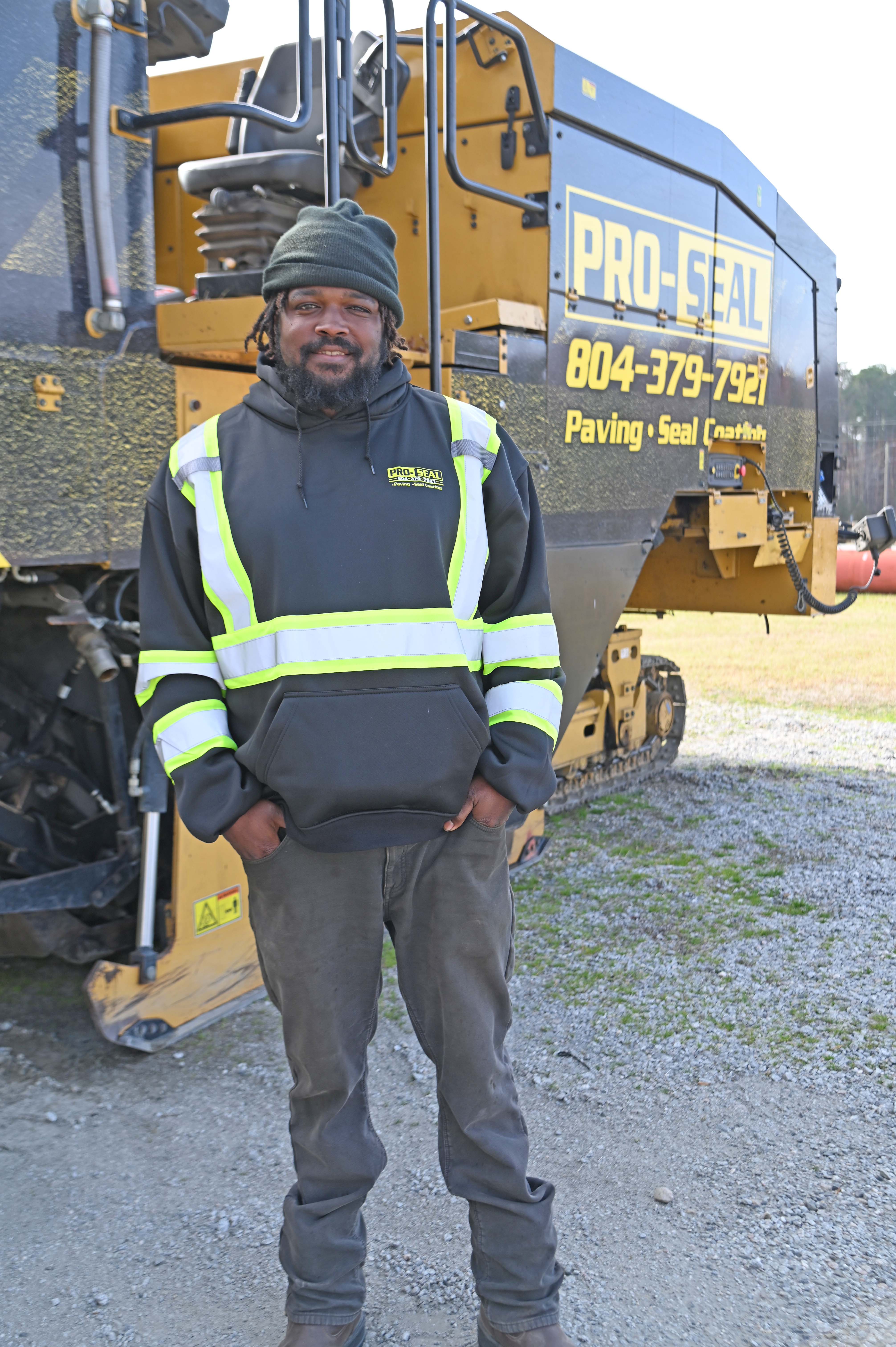 Phillip Rowe standing in reflective gear in front of paving equipment